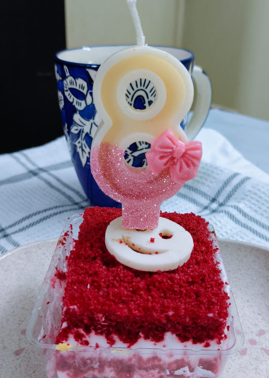 Red velvet cake with a number 8 candle in front of a blue mug on a table.