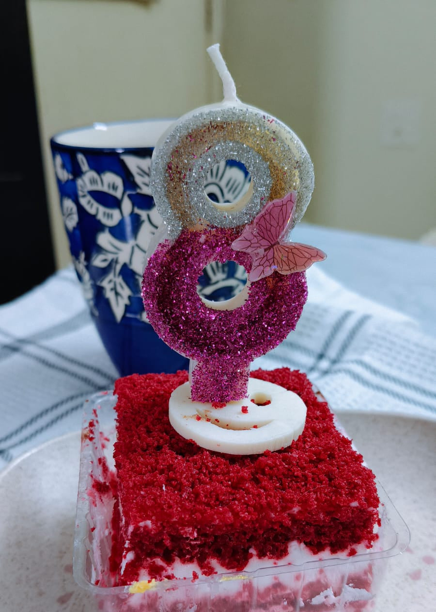 Small red velvet cake with a decorative candle on a white plate.