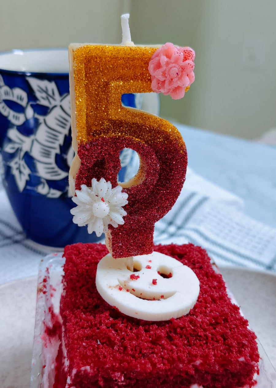 Red velvet cake with a number 5 candle on a white plate.