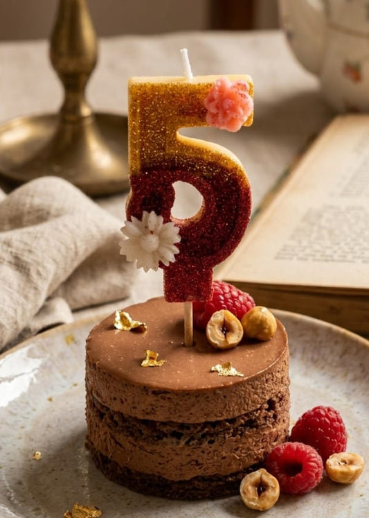 Small chocolate cake with a number 5 candle on a plate, surrounded by raspberries and hazelnuts.