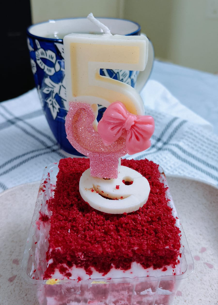 Red velvet cake with a number 5 candle on a white plate.