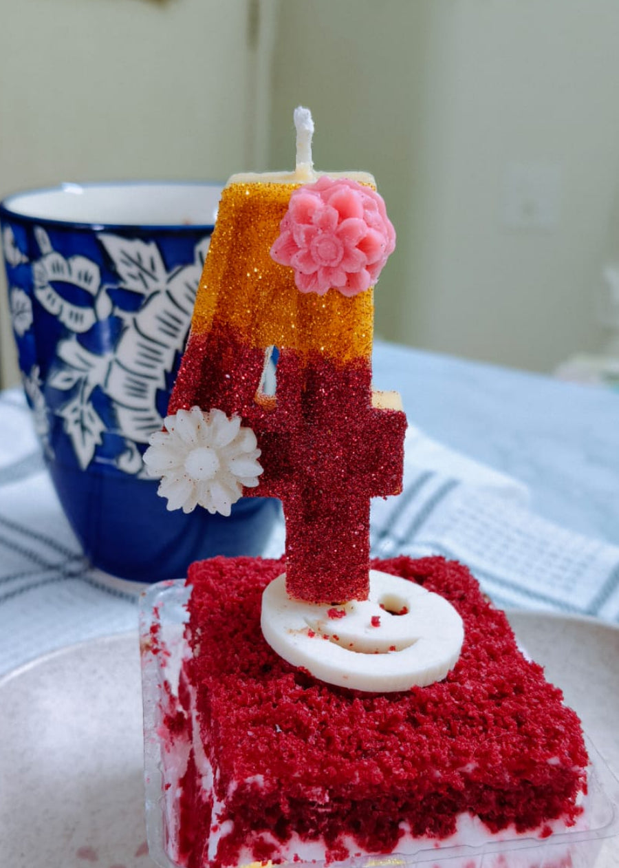 Red velvet cake with a number 4 candle on a white plate, with a blue mug in the background.