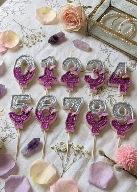 Decorative number candles on sticks with flowers and a box on a tablecloth.