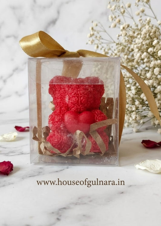Red teddy bear candle in a clear box with gold ribbon on a marble background