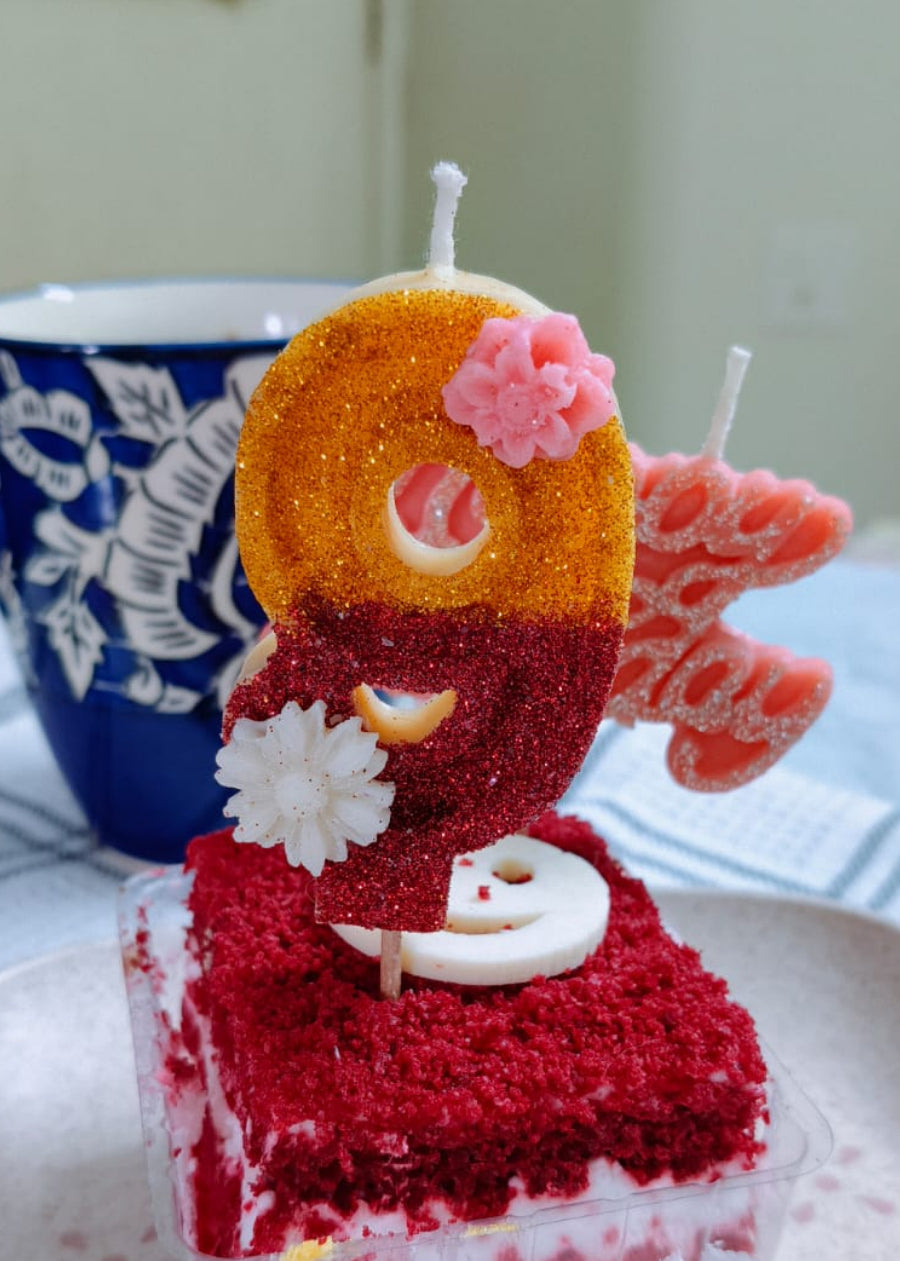 Red velvet cake with number 9 candle on a white plate, blue mug in the background