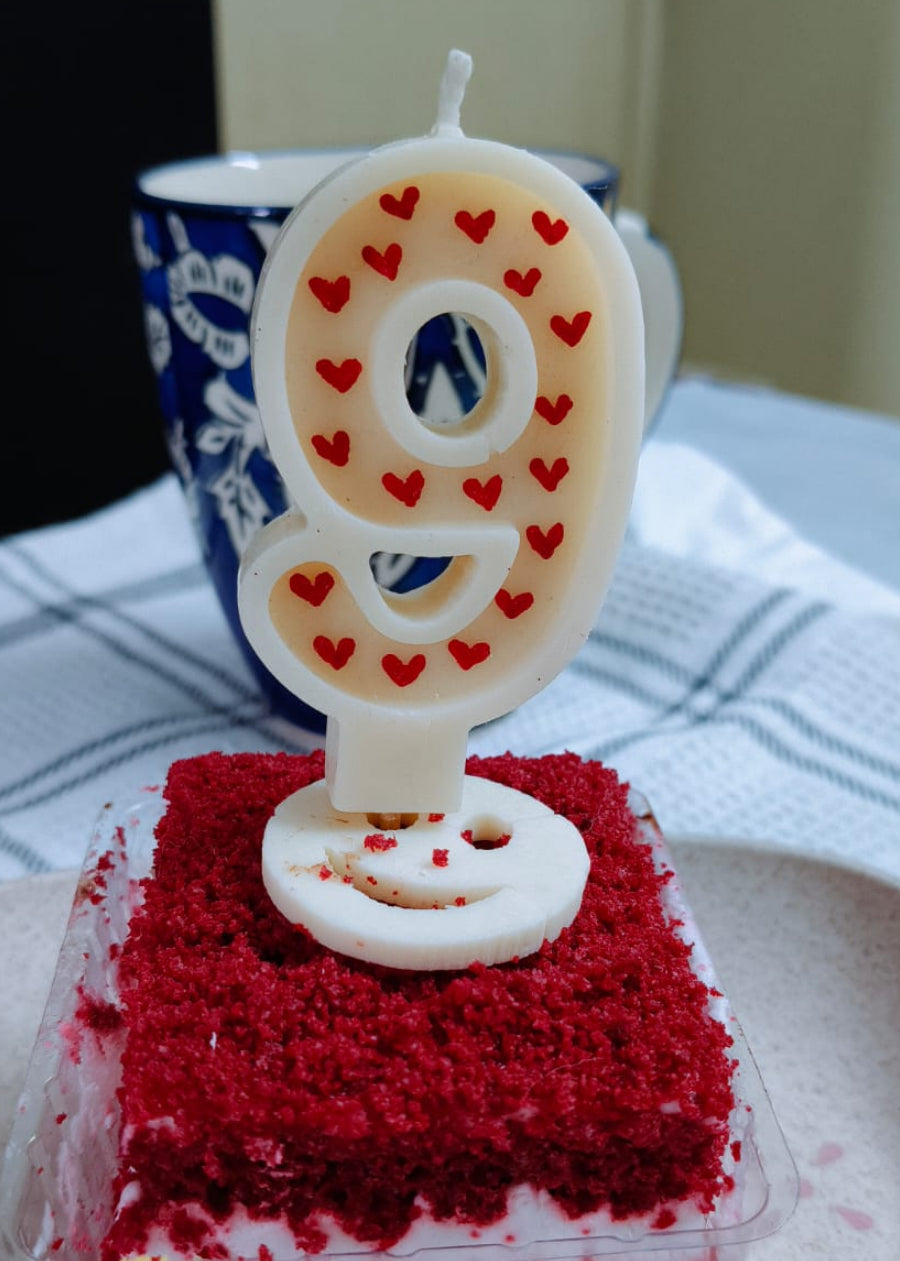 Small red velvet cake with a number 9 candle on a white plate.
