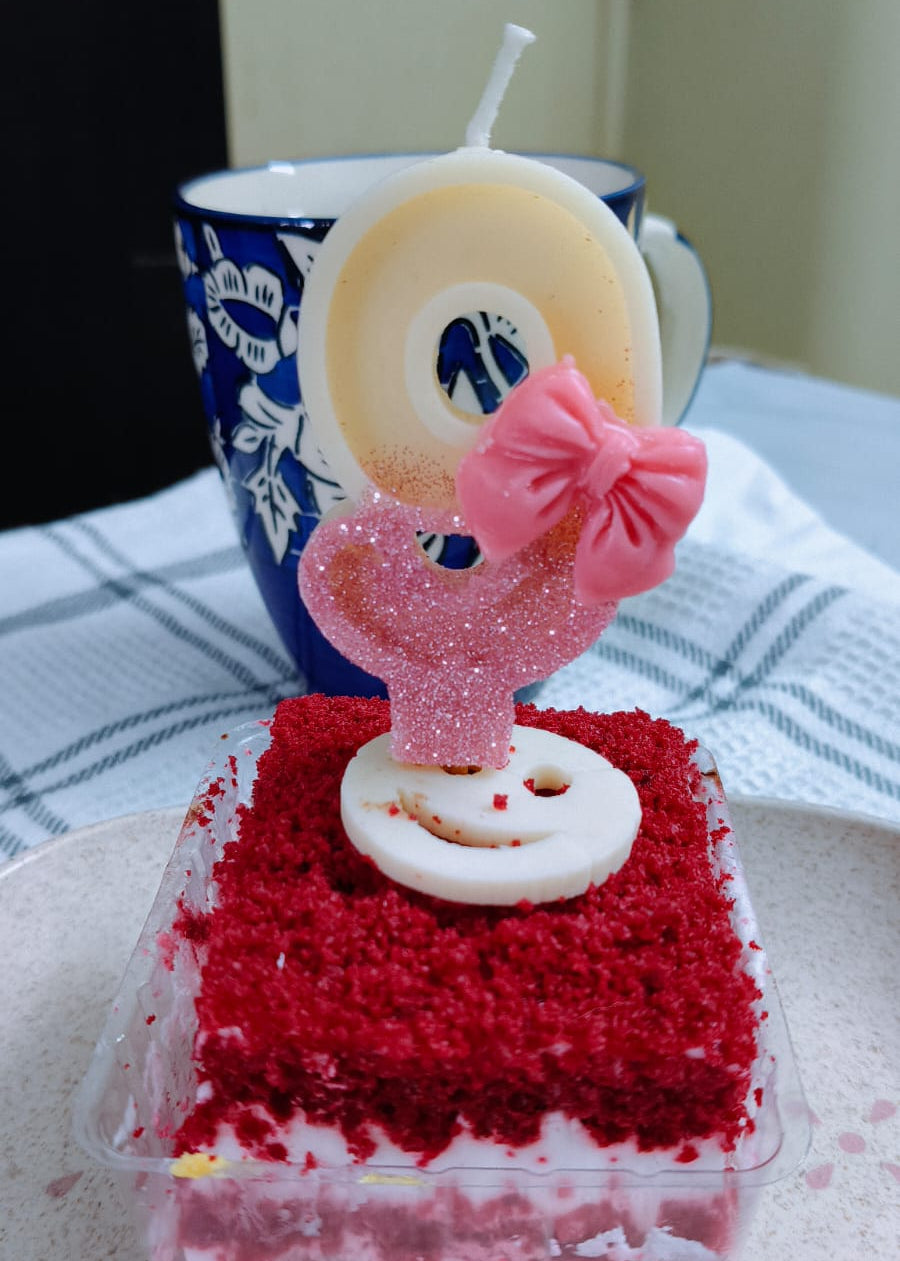 Small red velvet cake with a pink candle on top, next to a blue mug.
