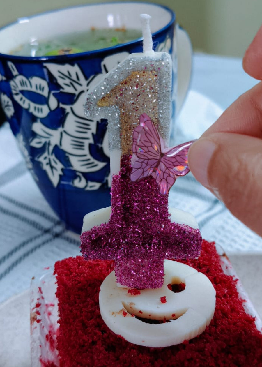 Red velvet cake with a number 1 candle, next to a blue and white mug.