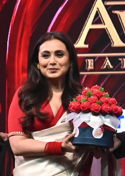 Rani Mukerjee bollywood actress in a red and white saree holding our candle bouquet on a stage with a red and gold background