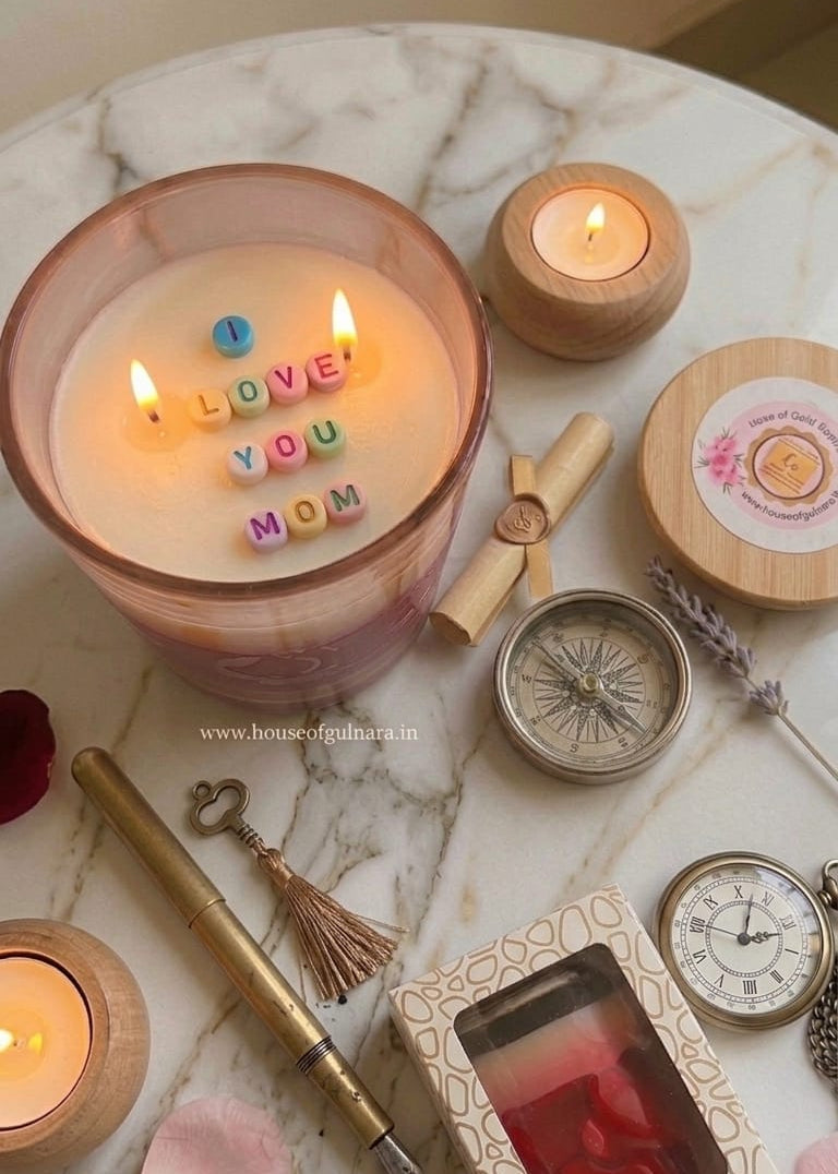 Candle with 'Love You Mom' message on a marble surface with decorative items.