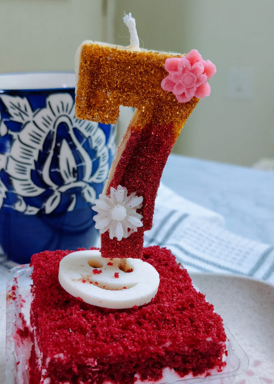 Red velvet cake with a number 7 candle on a white plate, with a blue mug in the background.