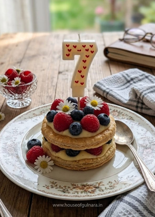 Small layered cake with berries on a plate, accompanied by a number 7 candle, on a wooden table.