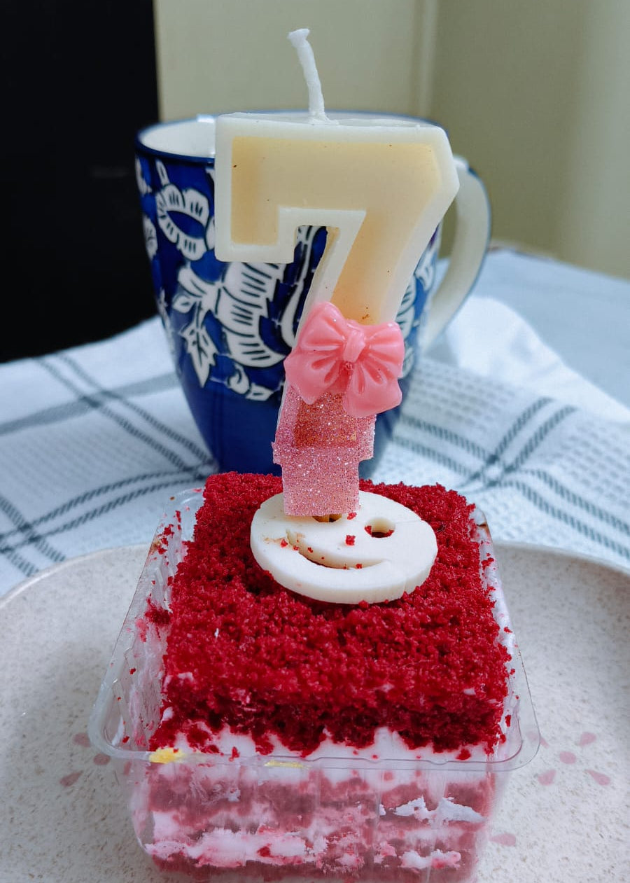 Small red velvet cake with a number 7 candle on a white plate.
