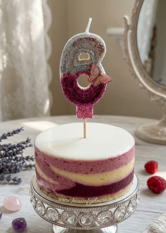 Small decorated cake with a number 6 candle on a decorative stand, surrounded by raspberries and lavender.