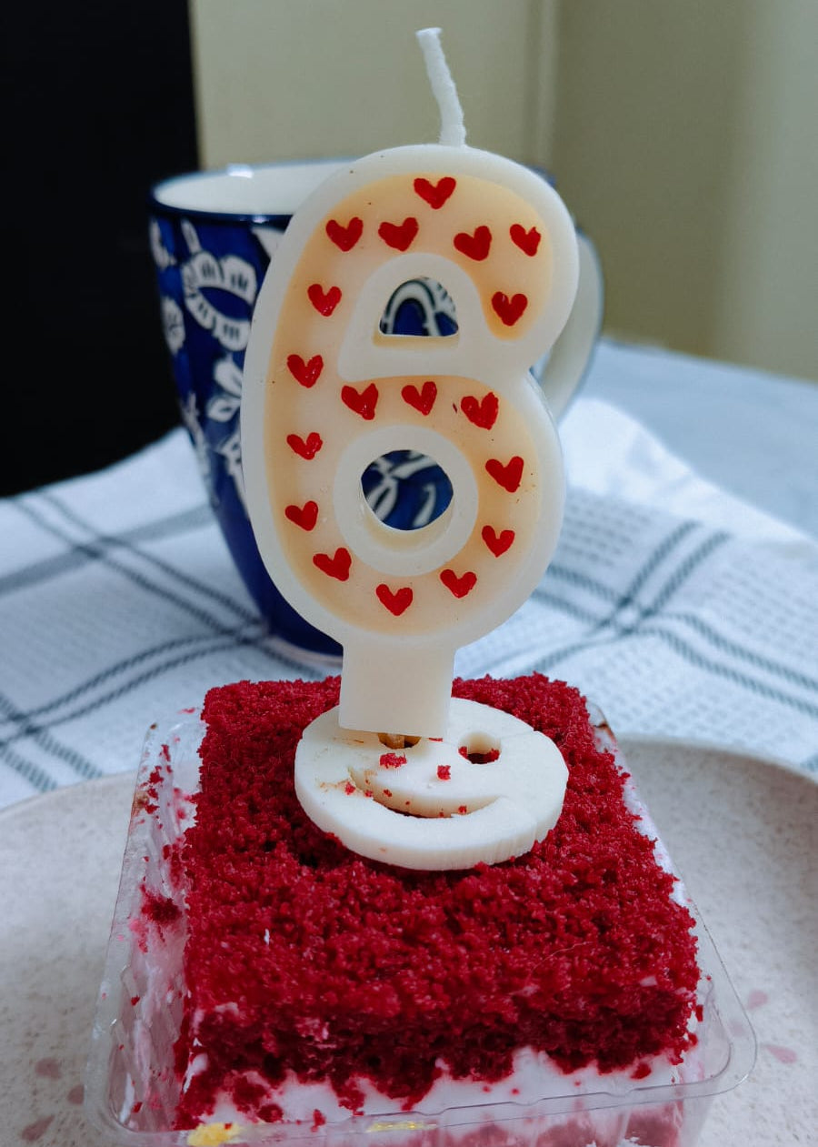 Red velvet cake with a number 6 candle on a white plate.