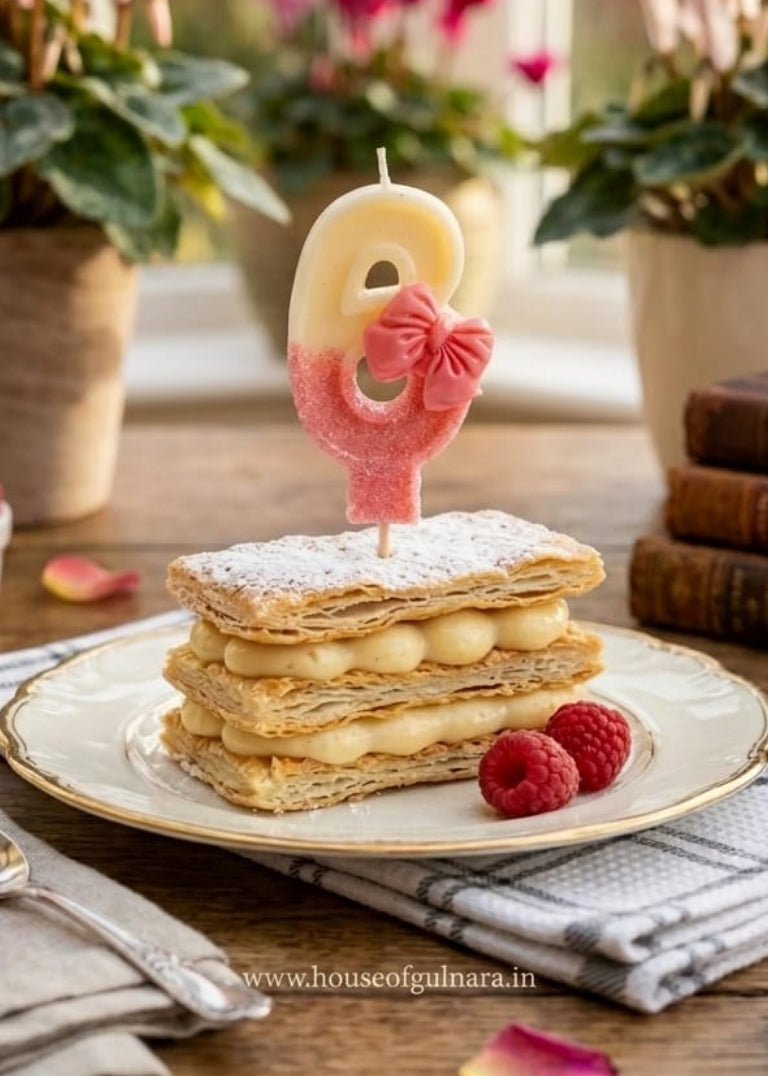 Decorative cake with a number 6 candle and pink bow, surrounded by flowers and raspberries on a wooden table.