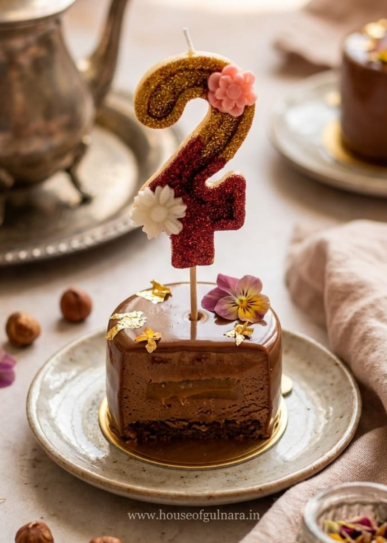 Small chocolate cake with a number 2 candle on a plate, surrounded by nuts and flowers.