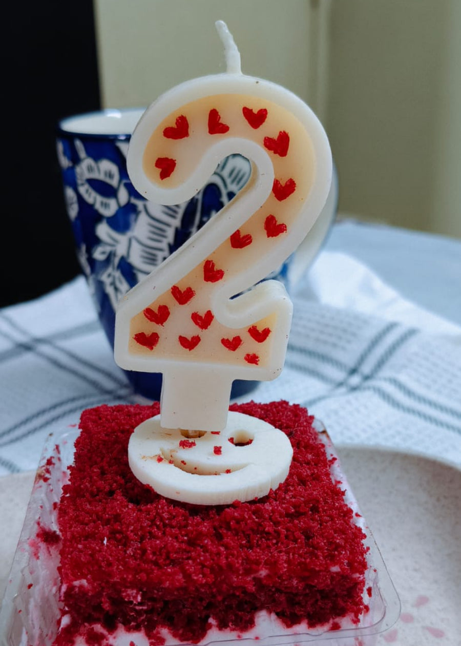 Small red velvet cake with a number two candle on a white plate.