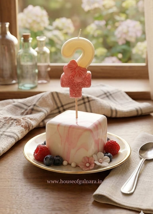 Small cake with a number two candle on a plate, set against a window with flowers in the background.
