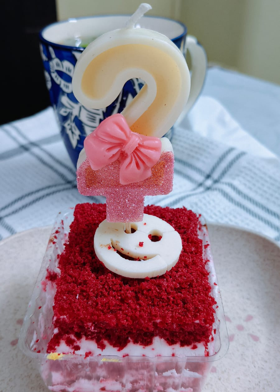 Small red velvet cake with a birthday candle and decorative topper on a white plate.