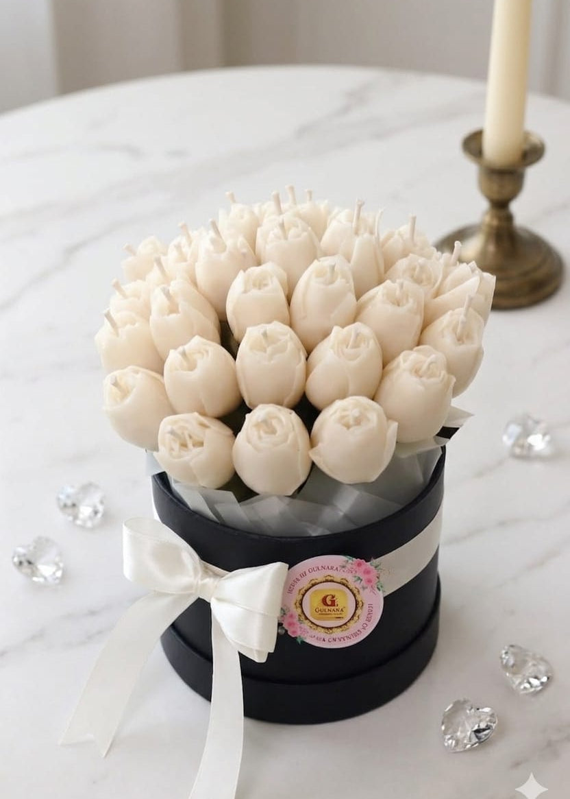 White tulip candle arrangement in a black box with decorative elements on a marble surface.