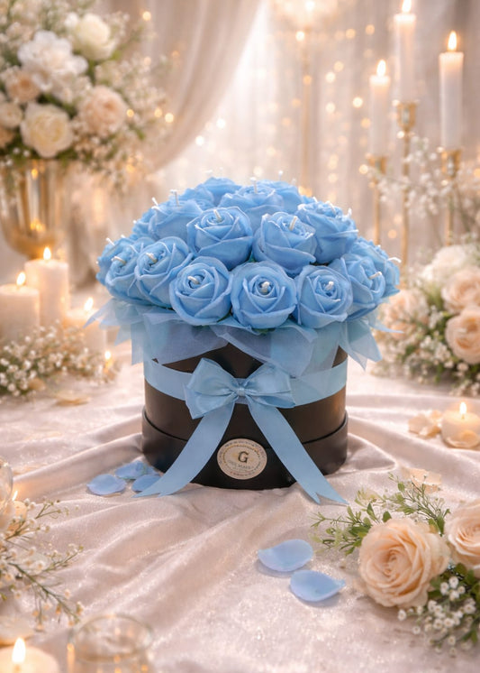Decorative box with blue roses and ribbons on a table with floral arrangements and candles.