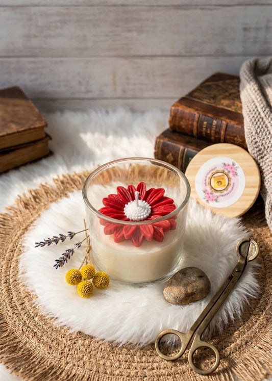 Glass candle with a red flower decoration on a textured surface with books and decorative items.
