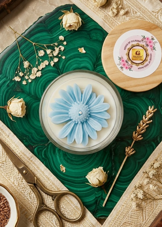 Decorative daisy candle with floral design on a textured surface with flowers and a book.