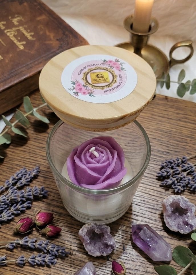 purple rose candle Decorative setup with a candle, glass with a flower, and crystals on a wooden surface.