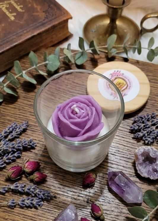 Rose Candle with a purple flower decoration on a wooden surface with books, lavender, and crystals.