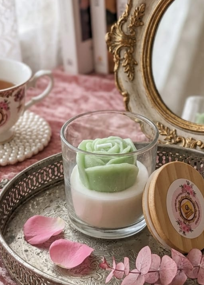 Tray with a small dessert, rose candle, and a teacup on a pink surface with a decorative mirror.
