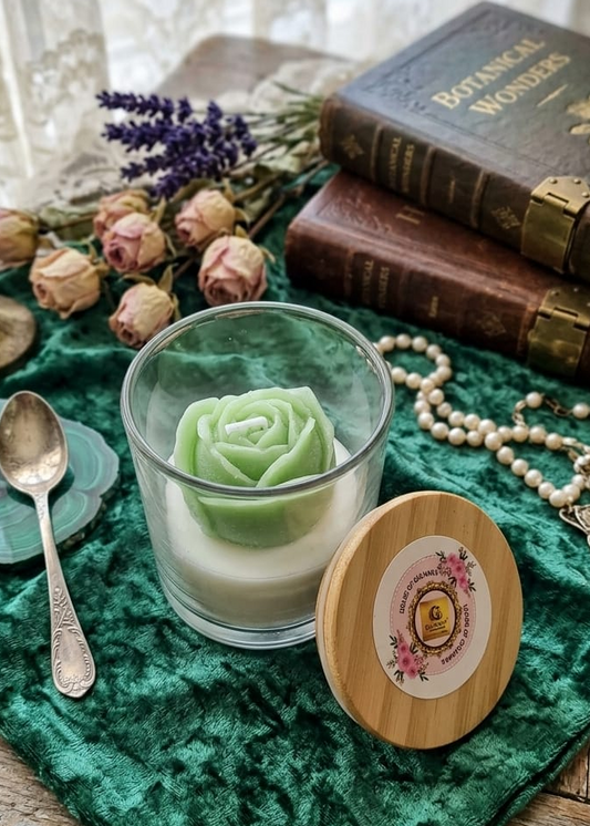 Green rose candle in a glass holder on a wooden table with books and flowers in the background