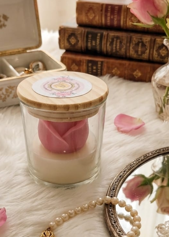 Candle with pink rose petals, vintage books, and decorative hand mirror on a textured surface.