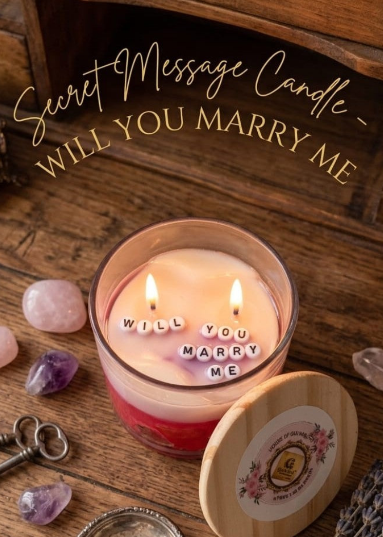 Candle with 'Will You Marry Me' message on a wooden surface with crystals and keys.