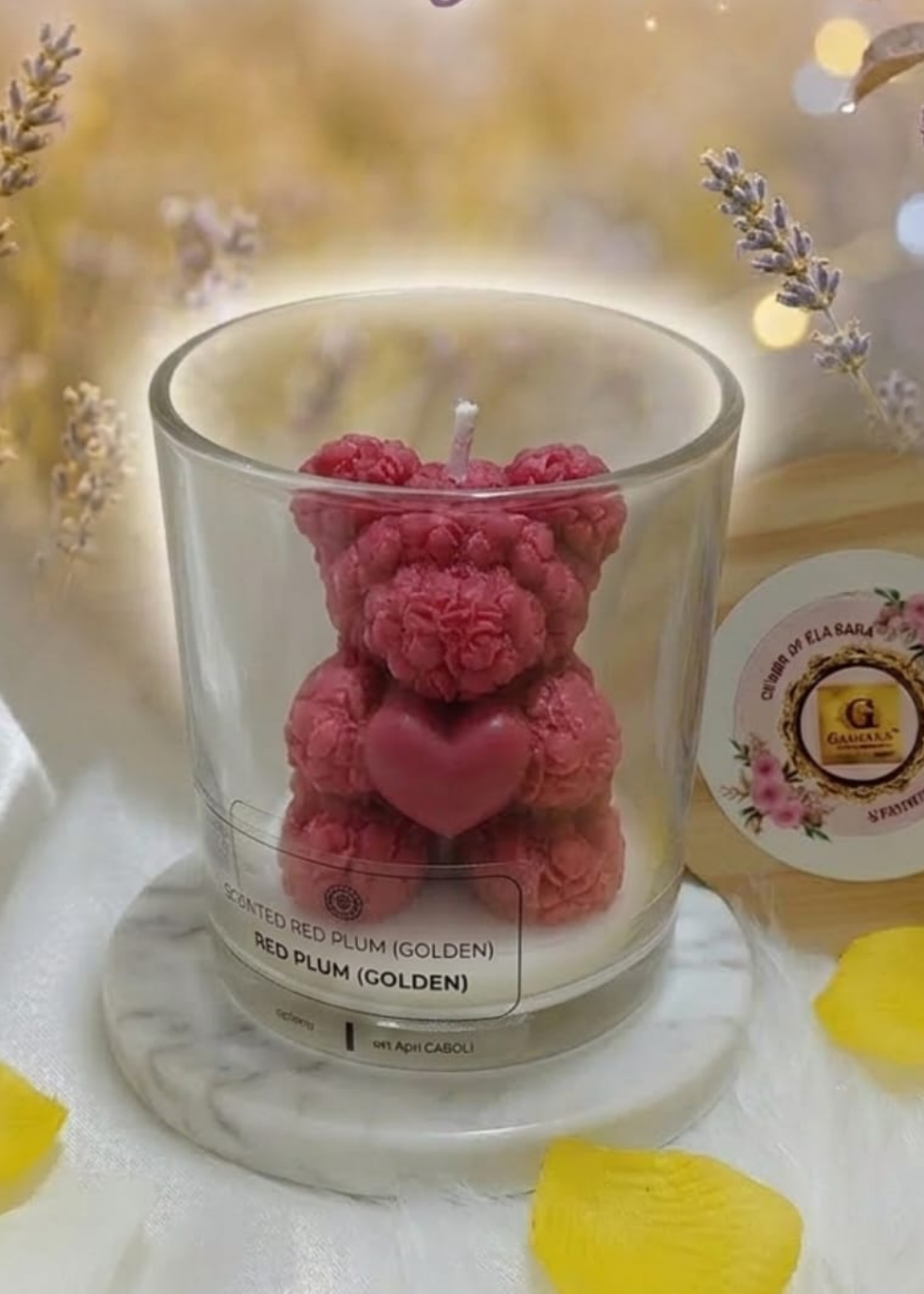 Candle shaped like a red plum teddy bear with decorative elements on a soft focus background