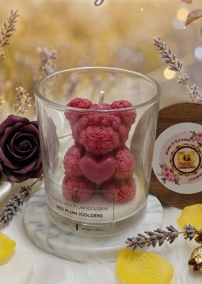 Glass candle with red plum teddy bear inside, surrounded by flowers and decorative elements on a soft background.
