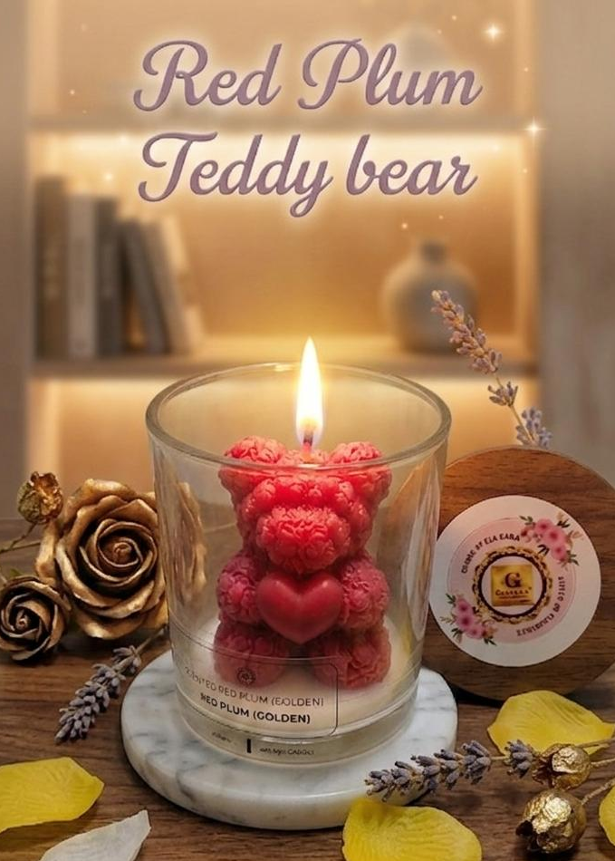 Candle in a glass jar with a red plum teddy bear design on a wooden surface with flowers.