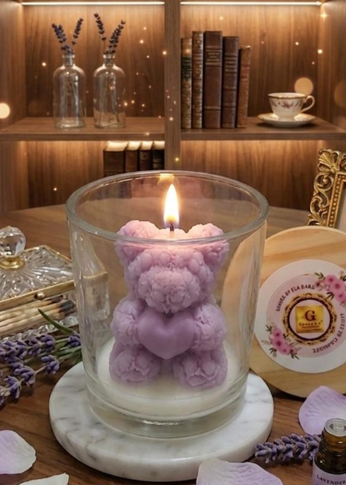 Candle with a purple teddy bear inside on a wooden surface with lavender and books in the background