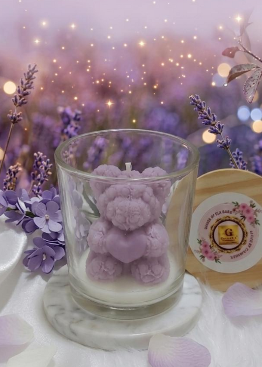 Candle with teddy bear design in a glass holder on a decorative surface with lavender flowers and lights.