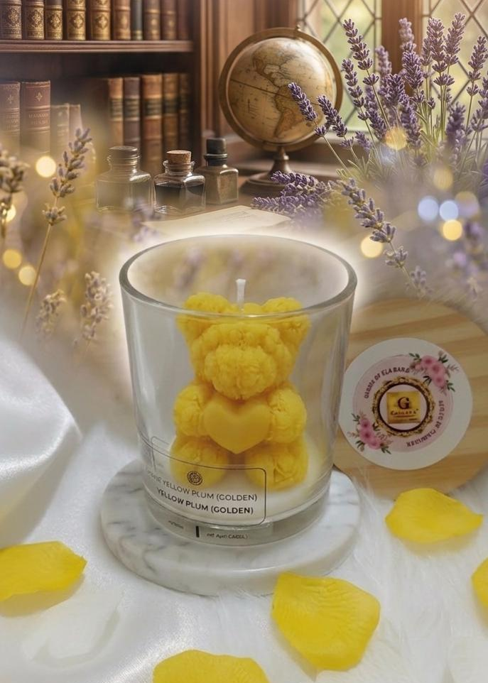 Yellow teddy bear candle in a glass jar on a decorative surface with books and flowers in the background.