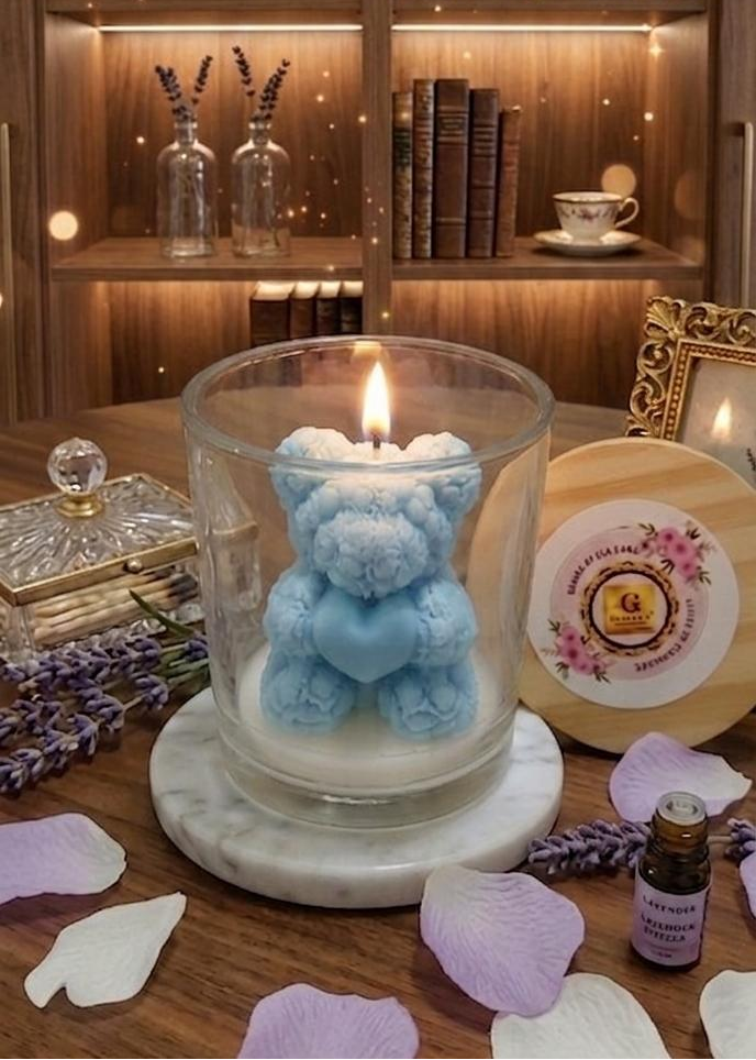 Candle in a glass holder with a blue teddy bear inside, on a wooden surface with decorative items.