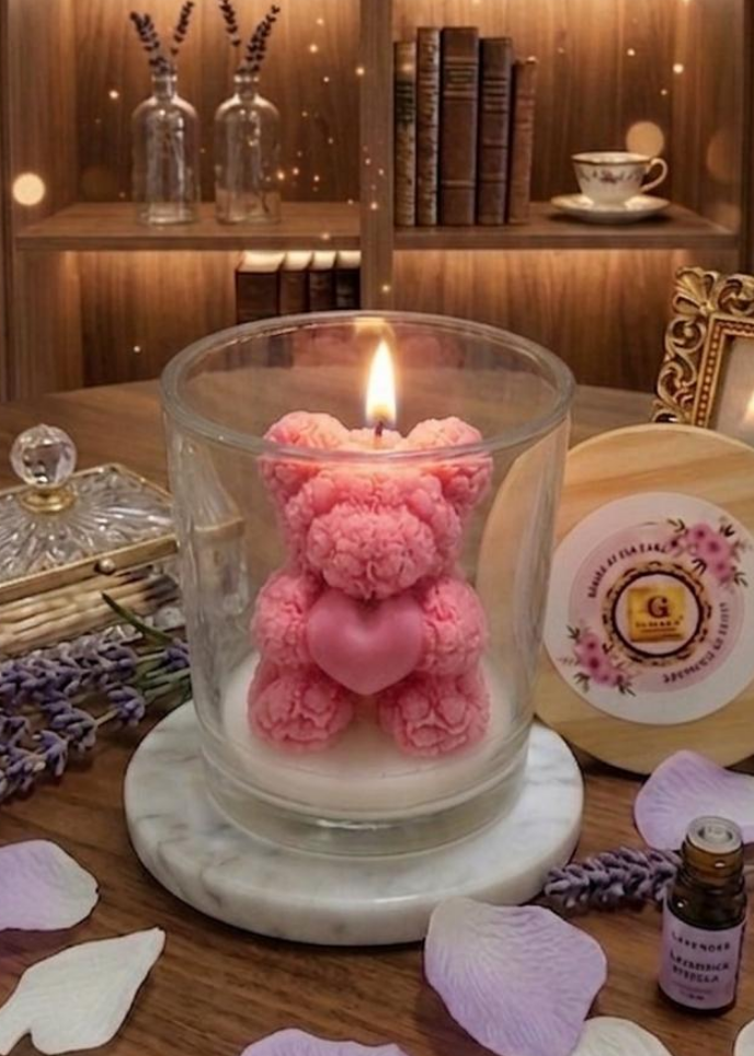 Pink teddy bear candle in a glass holder on a wooden surface with decorative elements.
