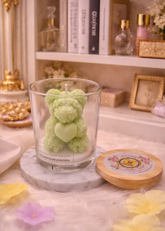 Green teddy bear candle in a glass jar on a decorative surface with books and decorative items in the background.