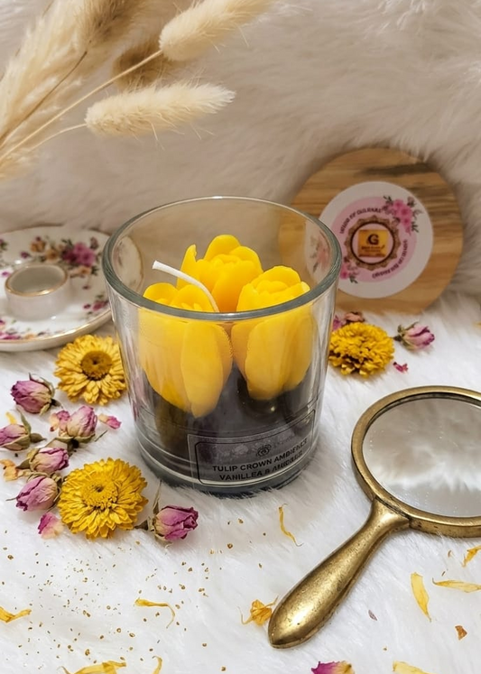 Glass with yellow TULIP candles on a surface with flowers and a magnifying glass.