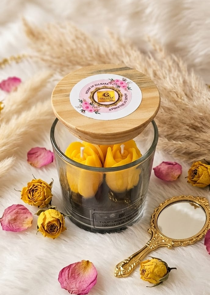 Glass jar with wooden lid containing yellow items, surrounded by dried flowers and a decorative mirror on a soft surface.