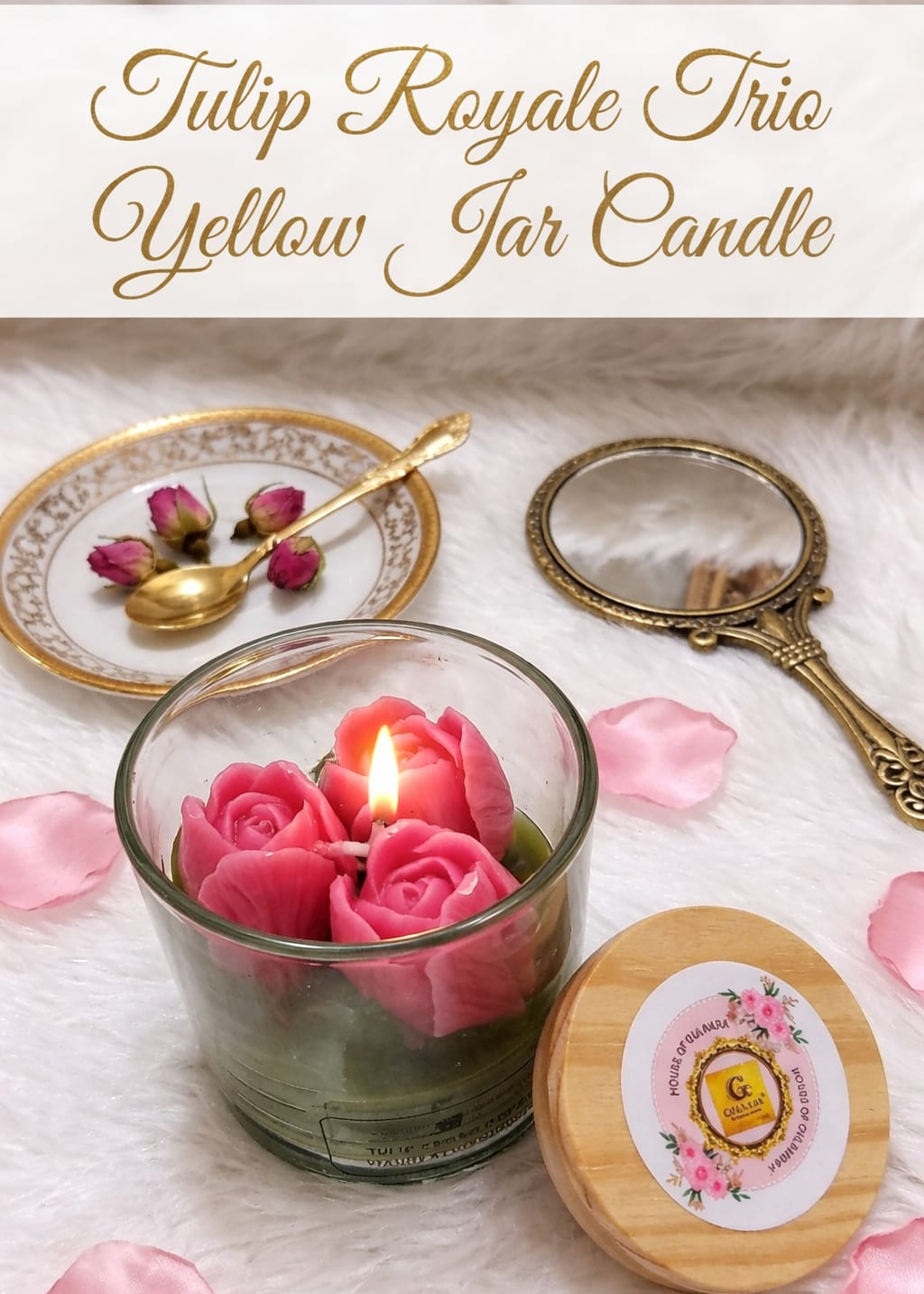Yellow jar candle with pink rose design, surrounded by rose petals and a decorative mirror on a white surface.
