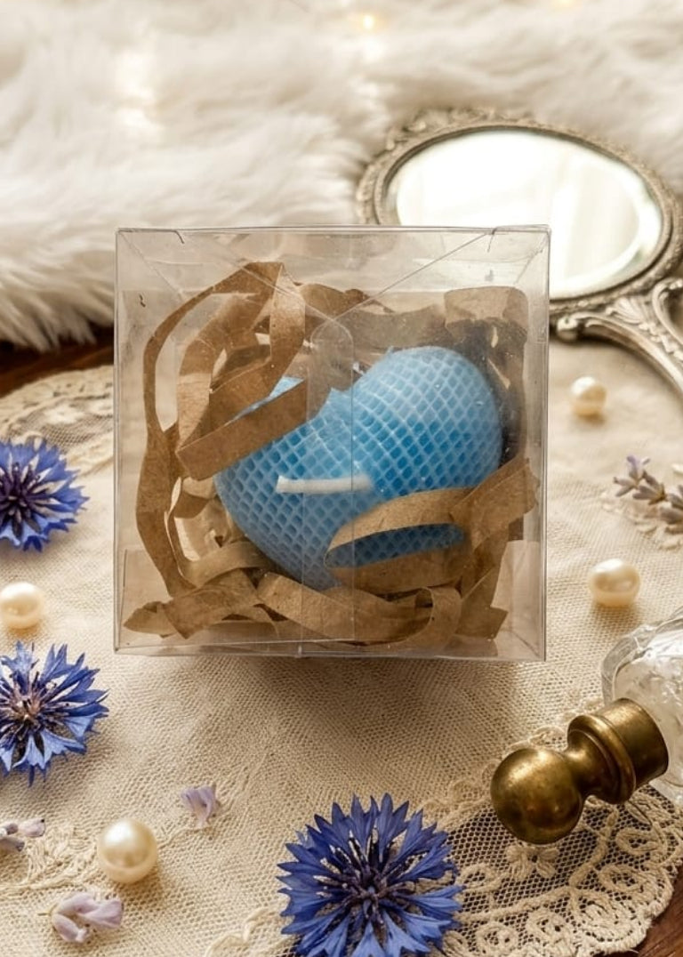 Blue textured object in a clear box on a lace surface with flowers and a mirror.