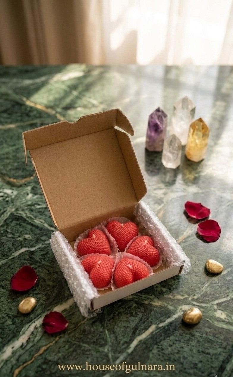 Red heart-shaped candles in a box on a marble surface with crystals and rose petals.