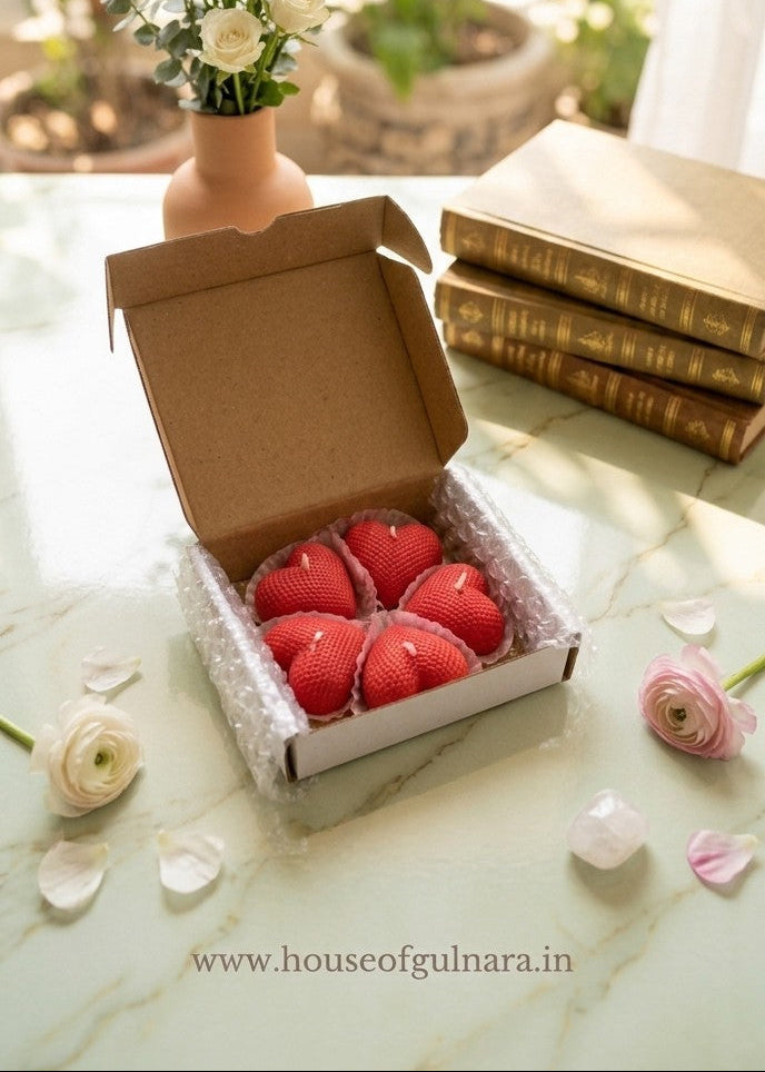 Box of red candles on a marble surface with flowers and books in the background