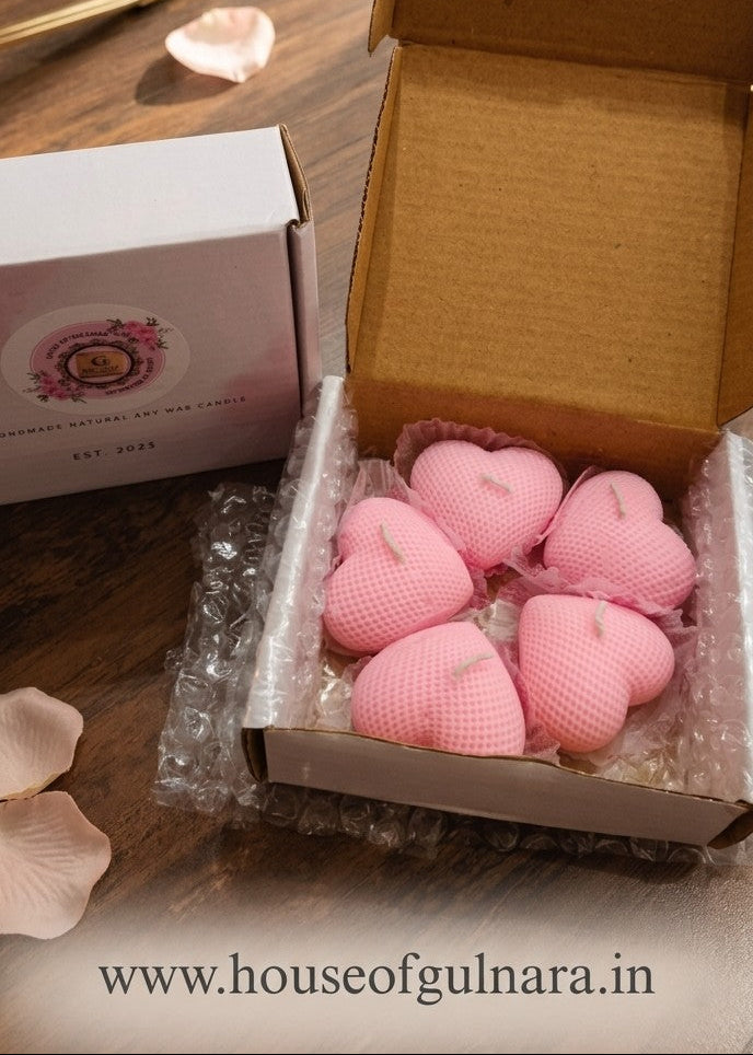 Box of pink knitted heart-shaped items on a wooden table with decorative elements.